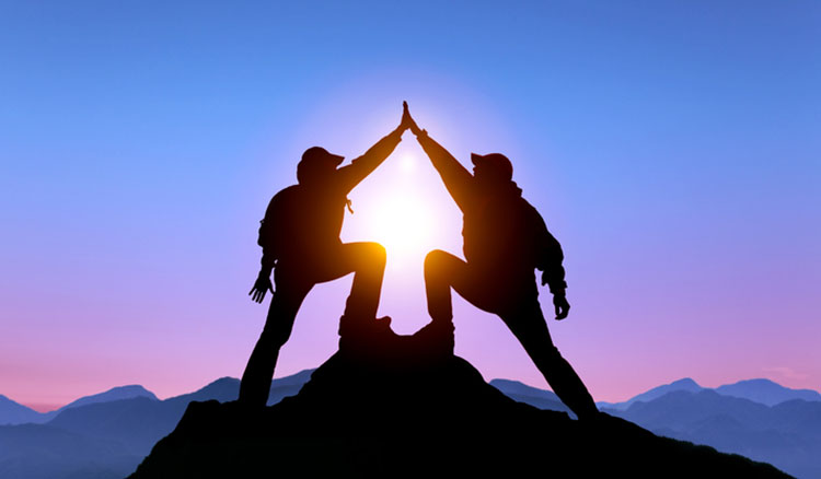 Two people standing on top of a mountain at daybreak